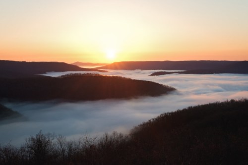 A serene sunrise over misty valleys, with rolling hills silhouetted against a colorful sky.