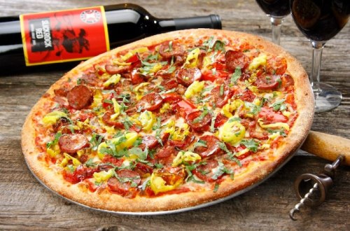 A delicious pizza topped with pepperoni, herbs, and colorful vegetables, accompanied by red wine in glasses.