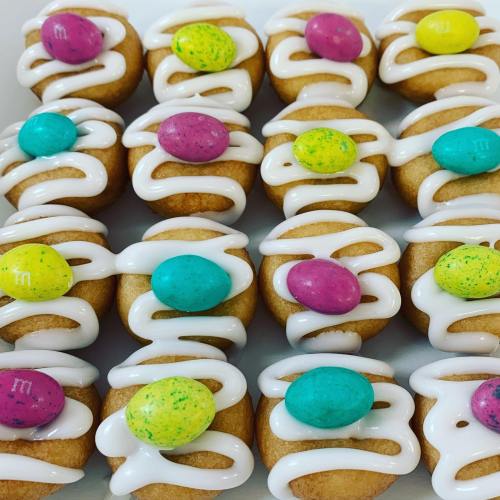 A tray of mini cakes topped with white icing and colorful candy eggs in pink, blue, and green.