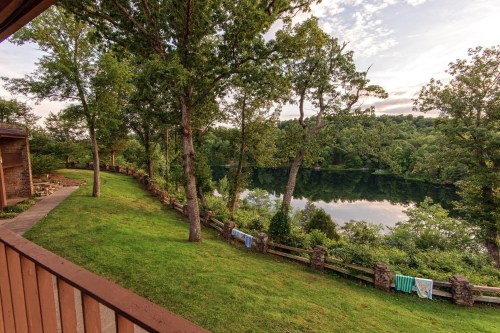 A serene lakeside view with lush greenery, trees, and towels hanging on a fence under a clear sky.