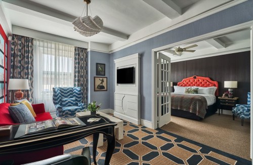 A stylish hotel room featuring a red chair, patterned rug, and a bed with a decorative headboard. Bright and modern decor.