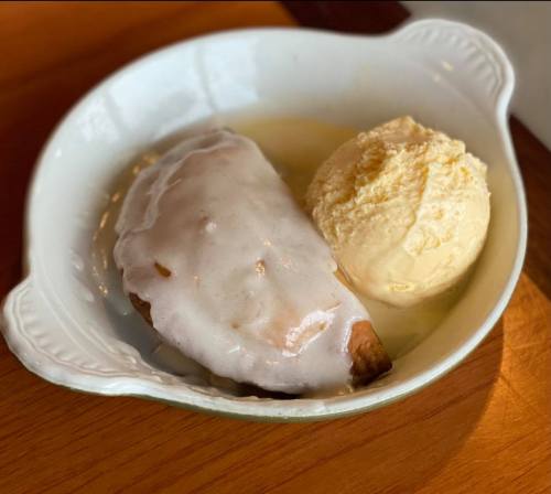 A bowl with a glazed pastry and a scoop of vanilla ice cream on a wooden surface.