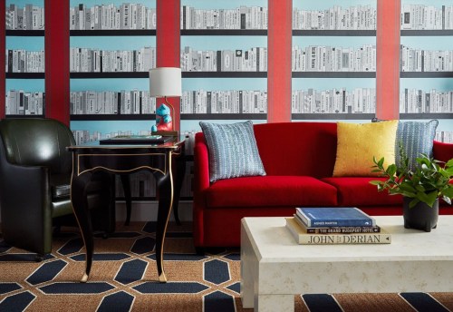 A cozy living room featuring a red sofa, patterned rug, and a bookshelf wallpaper backdrop.