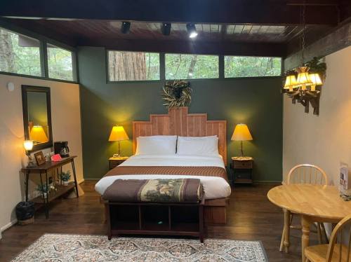 Cozy bedroom with a large bed, wooden decor, two lamps, a dining table, and large windows overlooking trees.