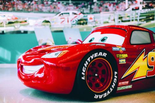 A close-up of a red cartoon race car with a smiling face, featuring the number 95 and "Lightyear" tires.