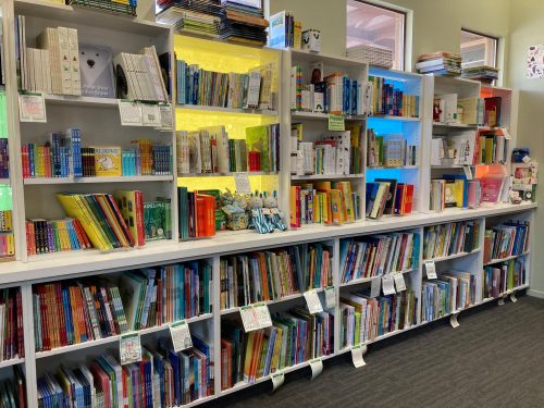 A colorful bookshelf filled with various books, organized by genre, in a well-lit library setting.