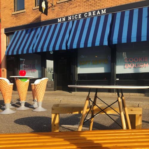 Outdoor seating in front of MN Nice Cream, featuring ice cream cones and a table, with a striped awning above.