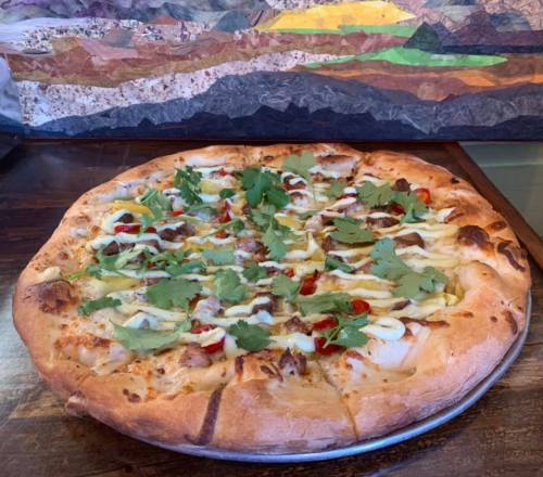 A freshly baked pizza topped with cilantro, red peppers, and drizzled with sauce, served on a wooden table.