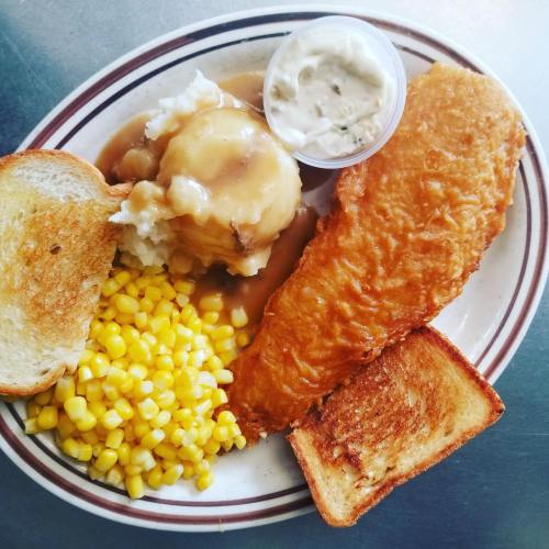 A plate of fried fish, mashed potatoes with gravy, corn, and toasted bread.