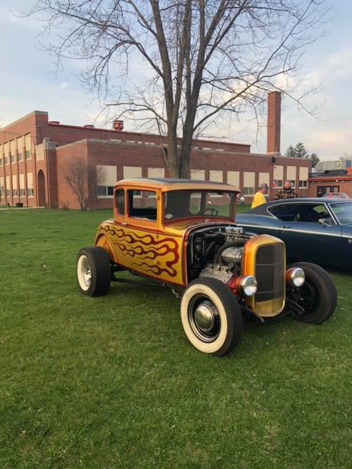 A vintage car with flame decals parked on grass, with a school building in the background.