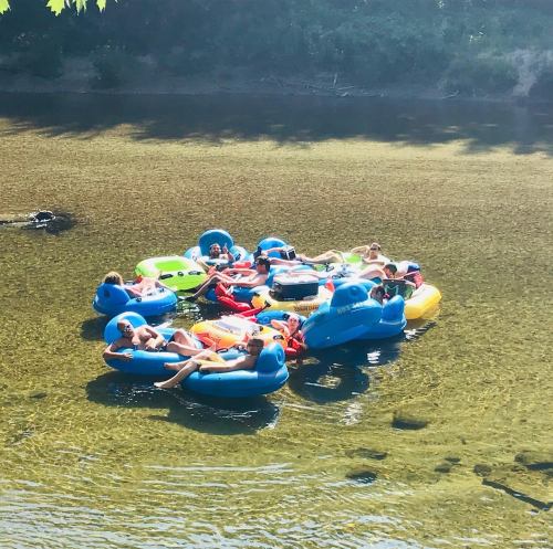 A group of people relaxing on colorful inflatable rafts in a shallow river, surrounded by greenery.