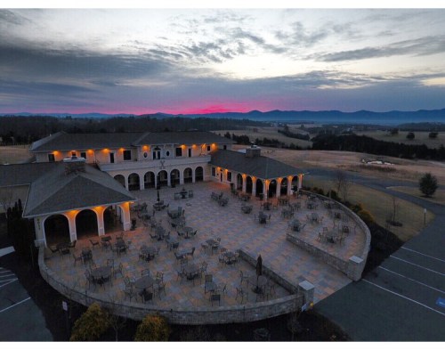 Aerial view of a spacious outdoor patio with tables, surrounded by mountains at sunset.