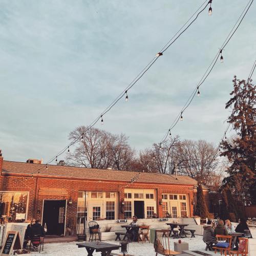 A cozy outdoor café with string lights, wooden tables, and patrons enjoying the ambiance under a cloudy sky.