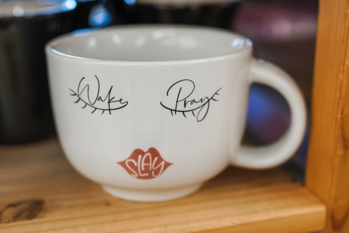 A white coffee mug with the words "Wake" and "Pray" and a red lip print on the front.