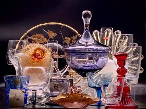 A collection of colorful glassware, including vases, bowls, and decorative pieces, arranged artistically against a dark background.