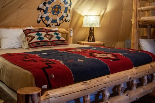 Cozy bedroom with a wooden bed, colorful blankets, and a lamp, featuring Native American-inspired decor.