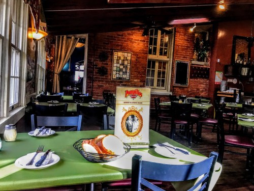 A cozy restaurant interior with green tables, a menu on display, and a basket of bread on the table.