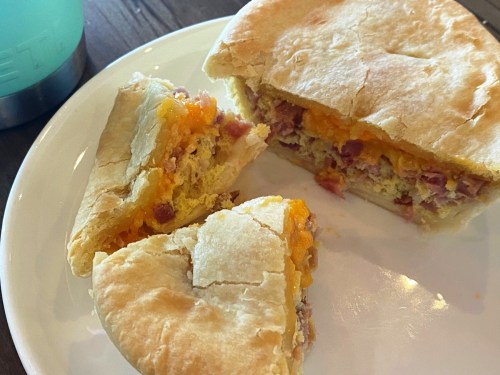 A plate with a sliced breakfast sandwich filled with eggs, cheese, and ham, alongside a drink in the background.