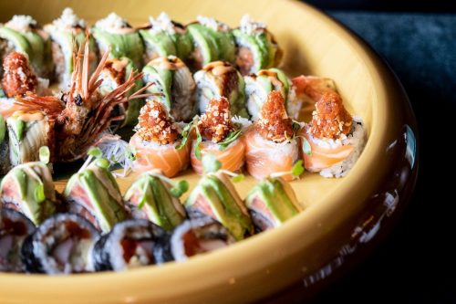 A colorful platter of assorted sushi rolls, featuring shrimp, salmon, and avocado, garnished with herbs.