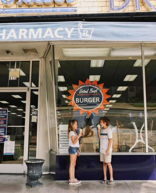 Two children stand outside a restaurant, holding drinks and smiling, with a "Voted Best Burger" sign in the window.
