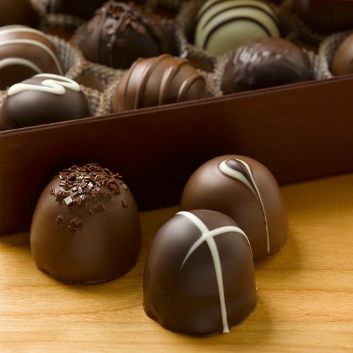 A variety of chocolate truffles in a box, featuring different designs and toppings on a wooden surface.