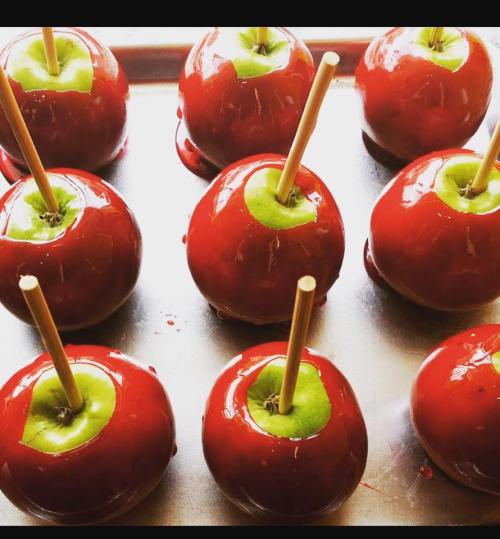 A tray of shiny red candy apples with green centers, each on a wooden stick.