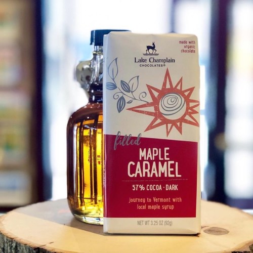 A box of Lake Champlain Chocolates filled maple caramel next to a bottle of maple syrup on a wooden surface.