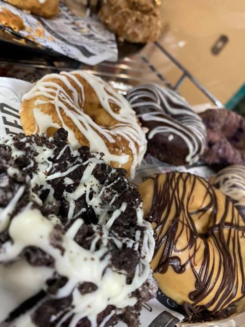 A close-up of assorted donuts topped with chocolate, white icing, and crushed cookies on a display tray.