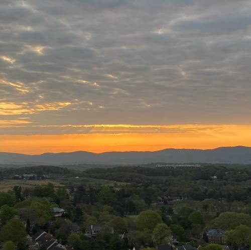 A serene landscape at sunset, with rolling hills and a cloudy sky illuminated by warm orange and yellow hues.