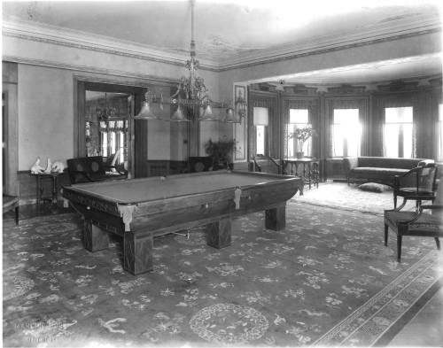 A vintage room featuring a billiard table, ornate chandelier, and elegant furnishings in a classic setting.