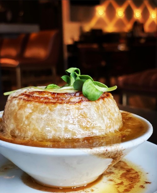 A close-up of a savory dish with a golden-brown crust, served in a white bowl, garnished with fresh greens.