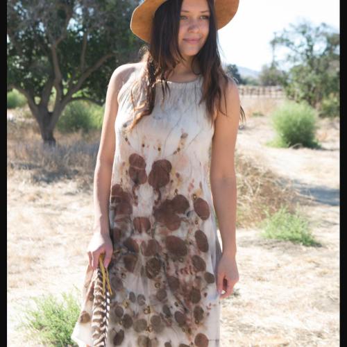 A young woman in a floral dress and wide-brimmed hat stands in a sunlit, grassy field.