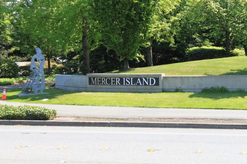Sign for Mercer Island with a sculpture nearby, surrounded by greenery and trees on a sunny day.
