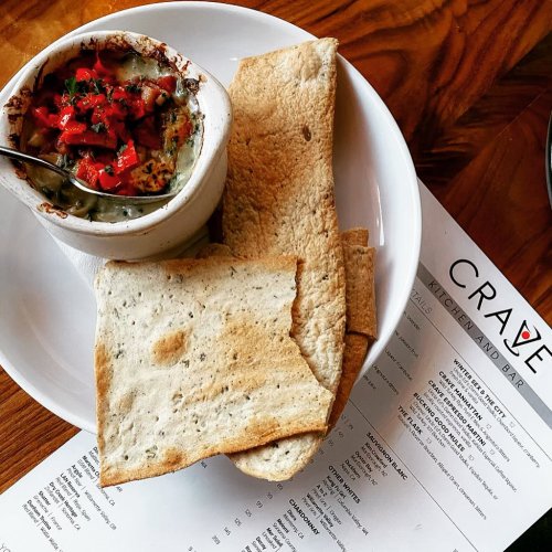 A bowl of baked dish topped with diced tomatoes, served with flatbread on a plate, alongside a menu.