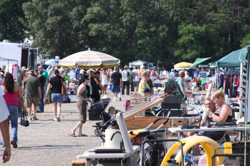 A bustling outdoor market with vendors, shoppers, and colorful umbrellas amidst various goods for sale.