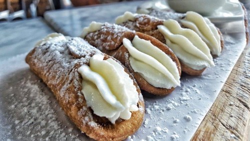 Three cream-filled pastries dusted with powdered sugar, arranged on a white plate.