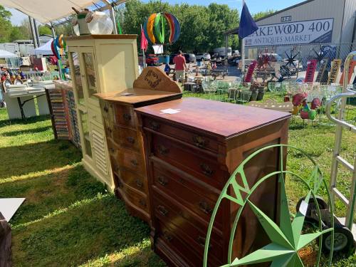 A variety of vintage furniture, including dressers and cabinets, displayed outdoors at an antiques market.