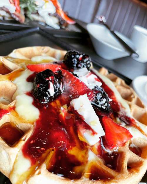 A close-up of a waffle topped with strawberries, blackberries, and a drizzle of berry sauce.
