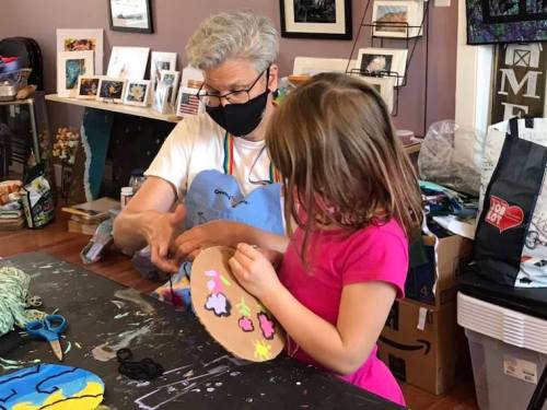 An adult and a child create art together, painting a colorful design on a craft project in a creative workspace.