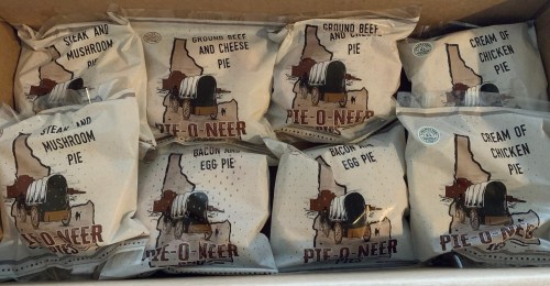 A box containing various packaged pies, including steak, mushroom, bacon, and cream of chicken flavors.