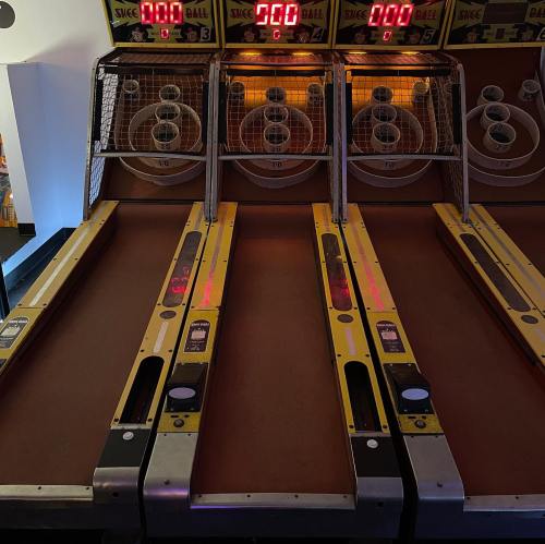Three skee ball lanes with scoreboards displaying zero points, illuminated in warm lighting.
