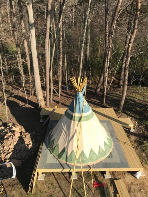 A colorful teepee on a wooden platform surrounded by trees in a natural setting.