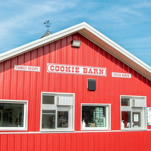 Red barn-style building with "Cookie Barn" sign, featuring windows and a weather vane against a blue sky.