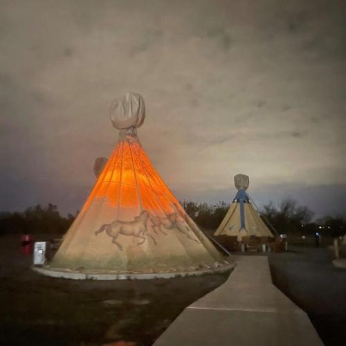 Two illuminated tipis at night, one featuring horse artwork, set against a cloudy sky.