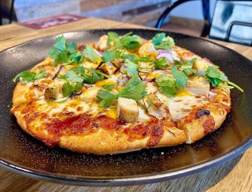 A close-up of a pizza topped with cheese, grilled chicken, red onions, and fresh cilantro on a black plate.