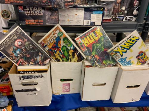 A collection of comic books displayed in white boxes, featuring titles like Spider-Man, Hulk, and X-Men.