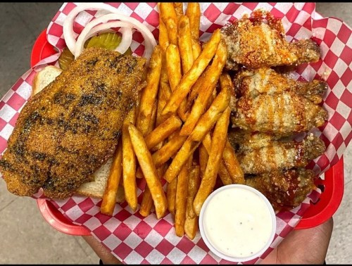 A red basket filled with seasoned fried fish, crispy chicken wings, French fries, pickles, onions, and dipping sauce.