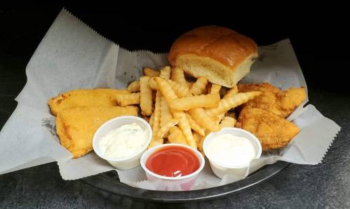 A plate of crinkle-cut fries, fried fish, chicken tenders, a bun, and dipping sauces on parchment paper.