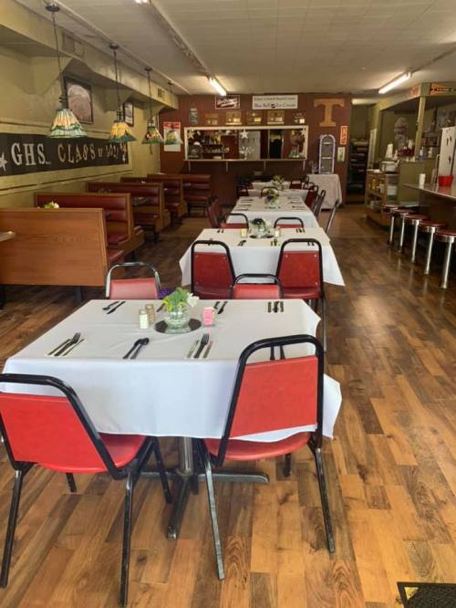 A cozy diner interior with red chairs, white tablecloths, and wooden floors, set for dining with simple decor.
