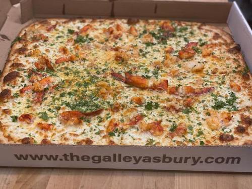 A large pizza topped with seafood, herbs, and cheese in a pizza box with a website printed on it.